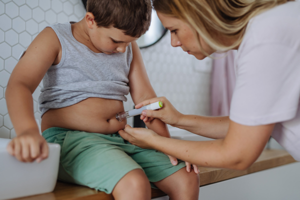 Mother of diabetic boy injecting insulin in his belly. Young boy with type 1 diabetes taking insuling with syringe needle in bathroom..