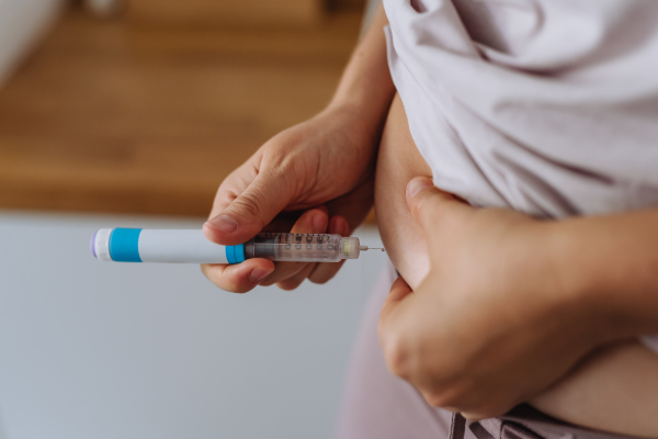 Close up of needle injecting insulin in abdomen in bathroom. Woman with type 1 diabetes taking insuling with syringe needle.