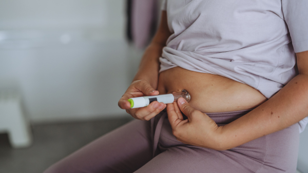 Woman injecting insulin with insulin pen in her abdomen in bathroom. Close up of mother with type 1 diabetes taking insuling with syringe needle.