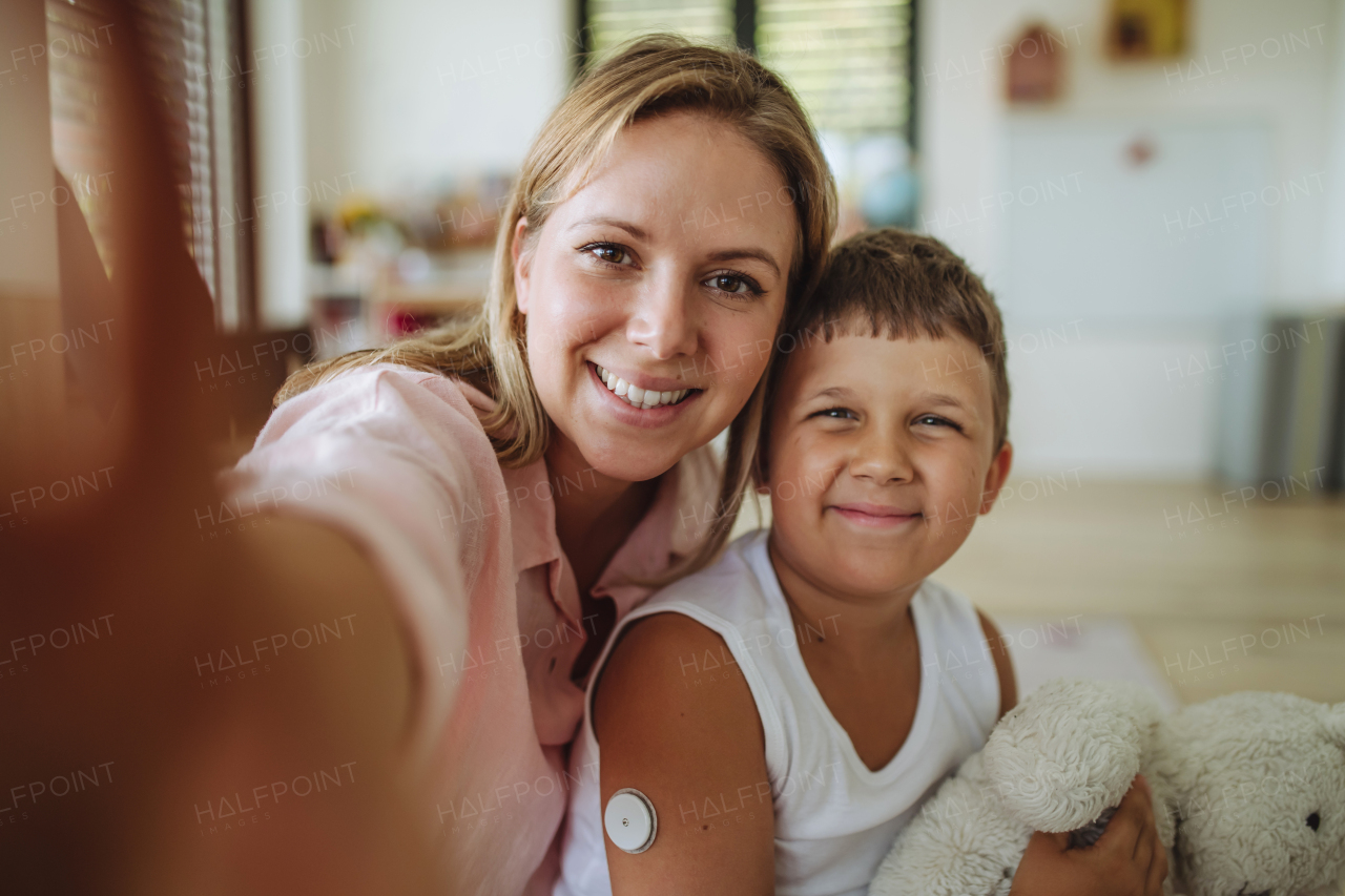 Selfie portrait of mother and diabetic boy with a continuous glucose monitor on his arm. The CGM device makes the life of the schoolboy easier, helping manage his illness and focus on other activities.