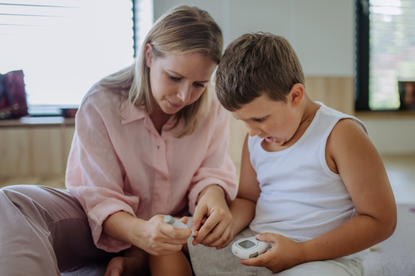 Mother checking her son's blood glucose level at home using a fingerstick glucose meter. The diabetic boy waiting for results from his blood test. Mother caressing her son's cheek.