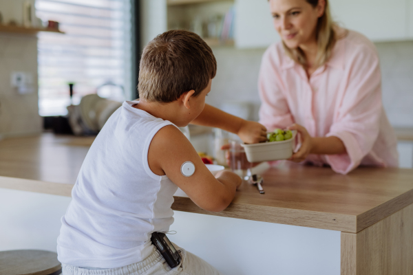 Diabetic boy with a continuous glucose monitor is careful with his diet. Mother checking what her son with diabetes eating. CGM device making life of school boy easier, helping manage his illness and focus on other activities.