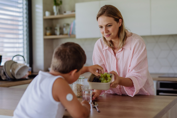 Diabetic boy with a continuous glucose monitor is careful with his diet. Mother checking what her son with diabetes eating. CGM device making life of school boy easier, helping manage his illness and focus on other activities.