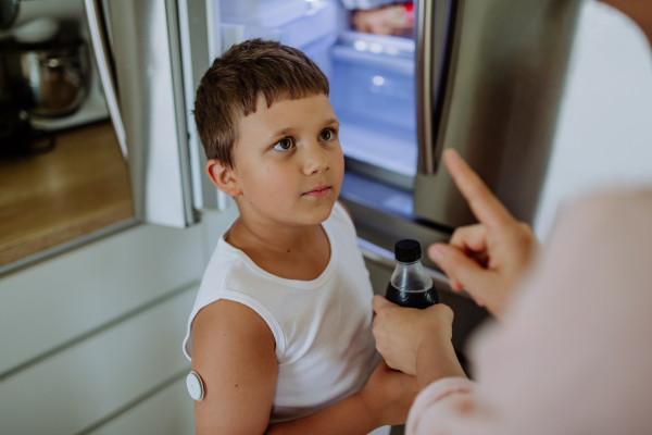 Diabetic boy with a continuous glucose monitor can't drink sweetened soda, sugar drink. Mother checking what her son with diabetes drinking.