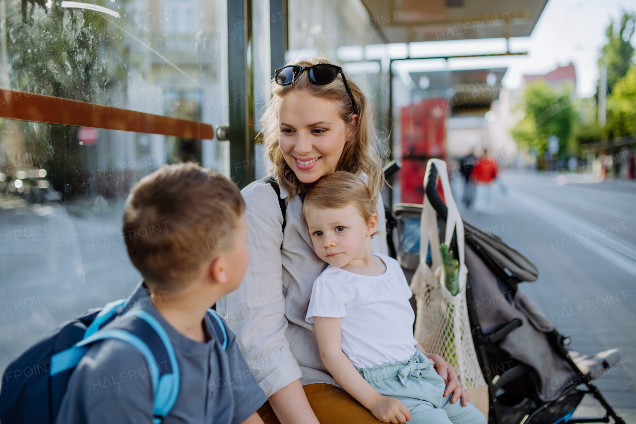 A young mother with little kids waiting on bus stop in city.