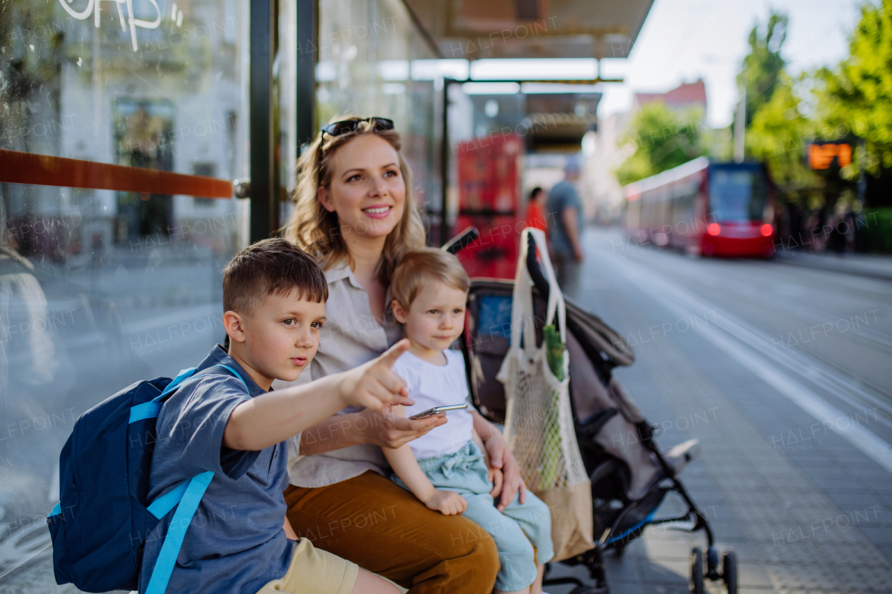 A young mother with little kids waiting on bus stop in city.