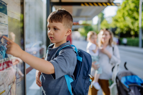 A young mother with little kids waiting on bus stop in city.