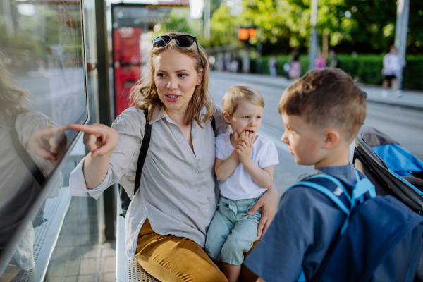 A young mother with little kids waiting on bus stop in city.