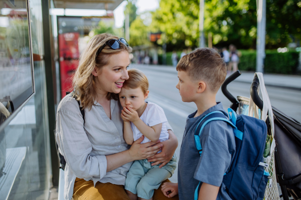 A young mother with little kids waiting on bus stop in city.