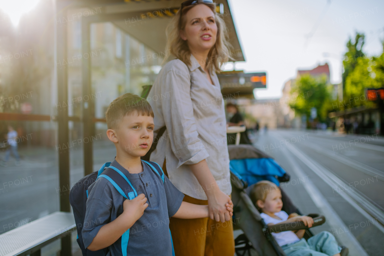 A young mother with little kids waiting on bus stop in city.