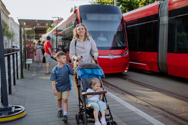 A young mother commuter with little kids on the way to school, walking on tram station in city.