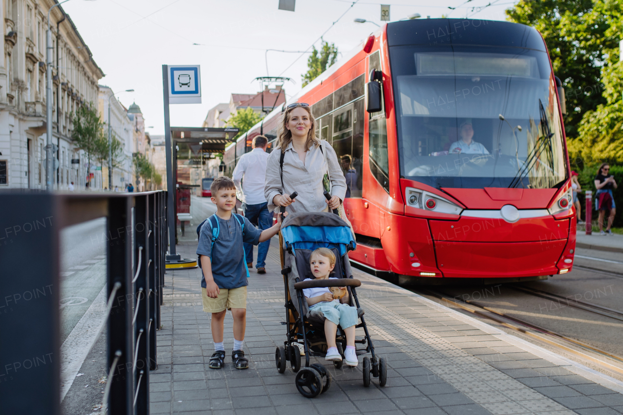 A young mother commuter with little kids on the way to school, walking on tram station in city.