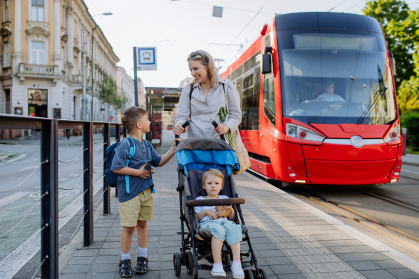 A young mother commuter with little kids on the way to school, walking on tram station in city.