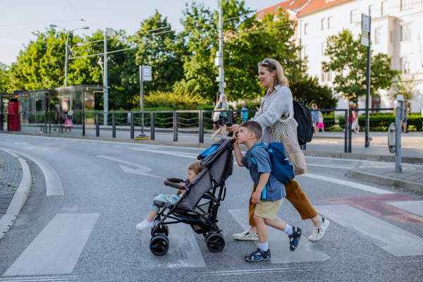 A young mother with zero waste shopping bag holding hands with her child and pushingstroller when walking in city street