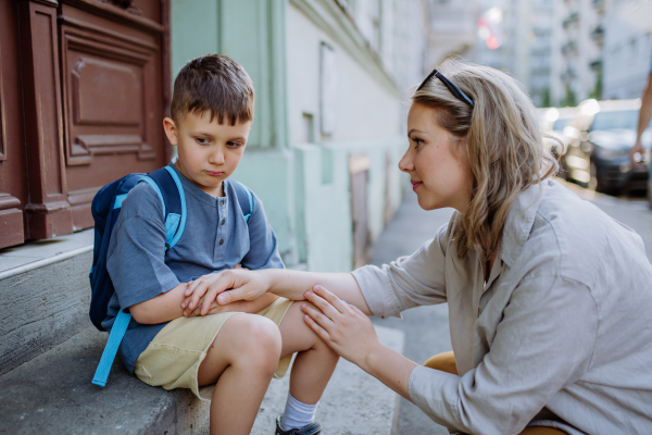 A mother consoling her little son on his first day of school,sitting on stair and saying goodbye before school.