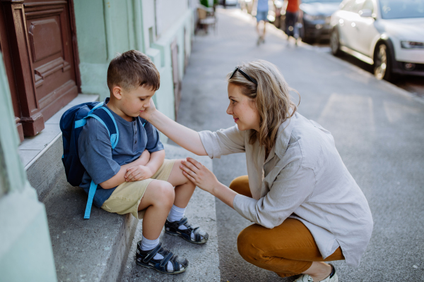 A mother consoling her little son on his first day of school,sitting on stair and saying goodbye before school.