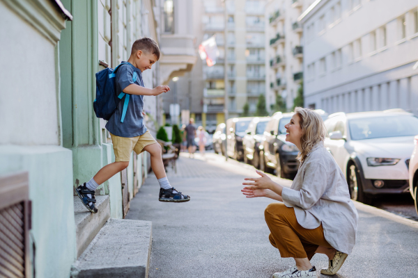 A young mother waiting for her little son on streetafter school, little boy is running to hug her.