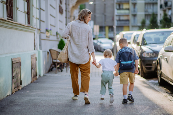 A young mother with zero waste shopping bag holding hands with her children and walking in city street street