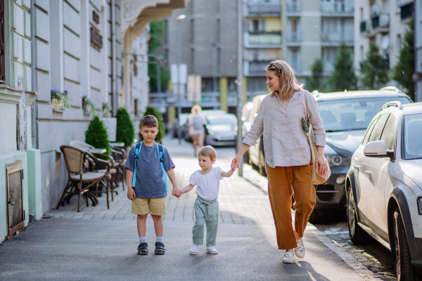 A young mother with zero waste shopping bag holding hands with her children and walking in city street