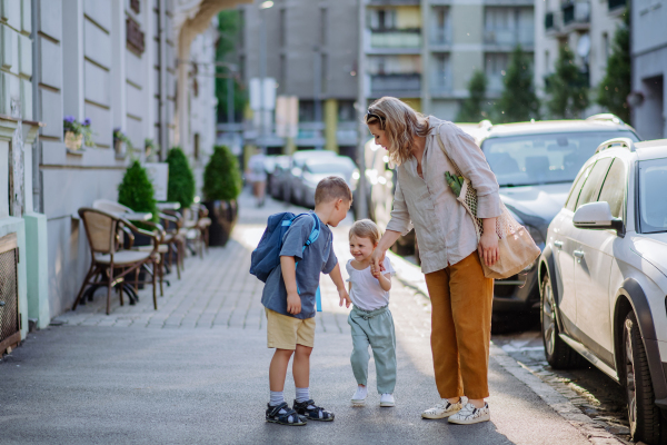 A young mother with zero waste shopping bag holding hands with her children and walking in city street street