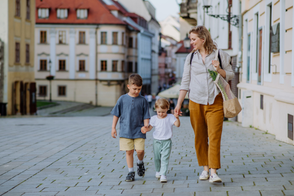 A young mother with zero waste shopping bag holding hands with her children and walking in city street street