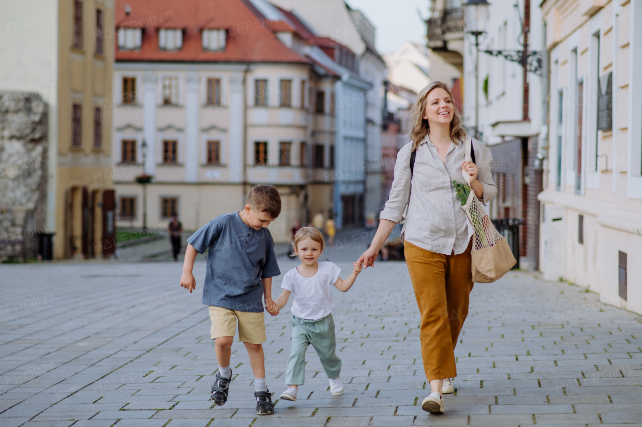 A young mother with zero waste shopping bag holding hands with her children and walking in city street street