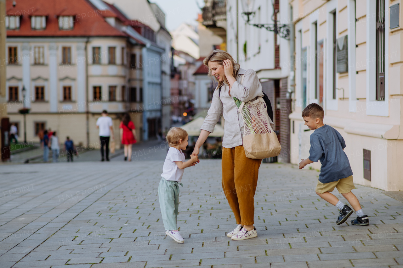 A young mother with zero waste shopping bag holding hands with her children and walking in city street street