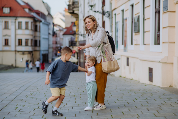 A young mother with zero waste shopping bag holding hands with her children and walking in city street street