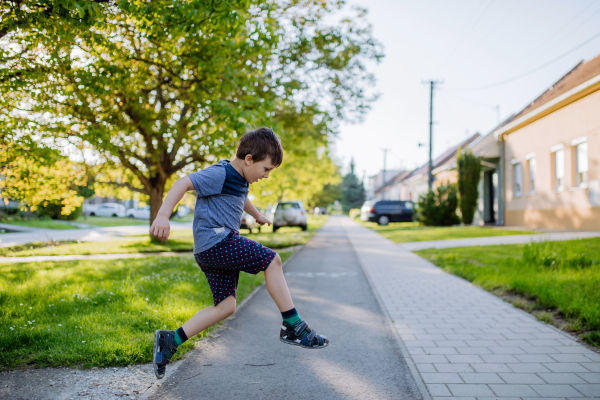 Little boy enjoying summer time outdoor on the street, jumping and smiling. Side view.