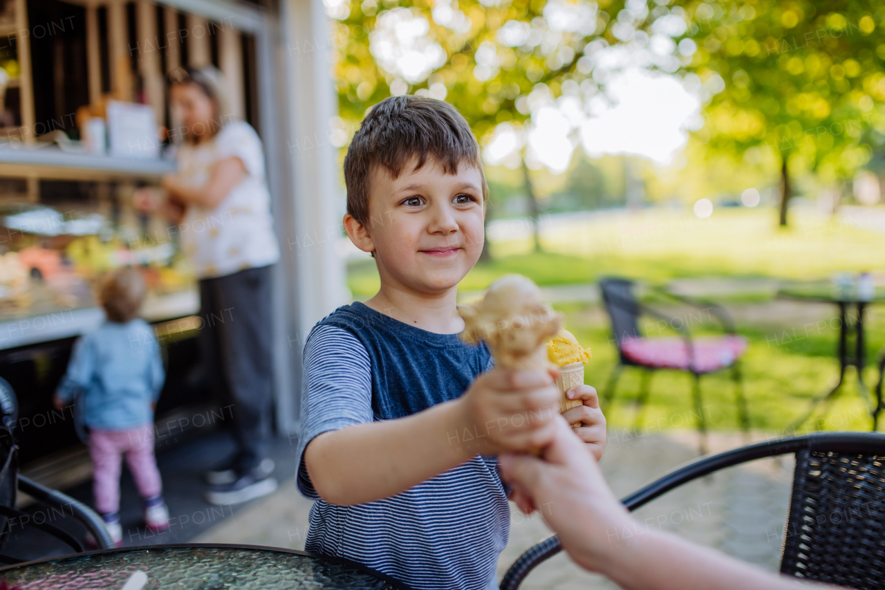 Little boy with his mum and sister enjoying an ice cream in park during hot summer day.