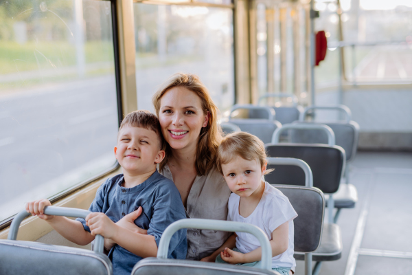 A young mother with little kids travelling in tram in summer, commuting and sustainable lifestyle concept.