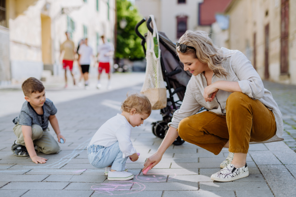 A little children with mother drwing with chalks on sidewalk in city on summer sunny day. Creative development of children.