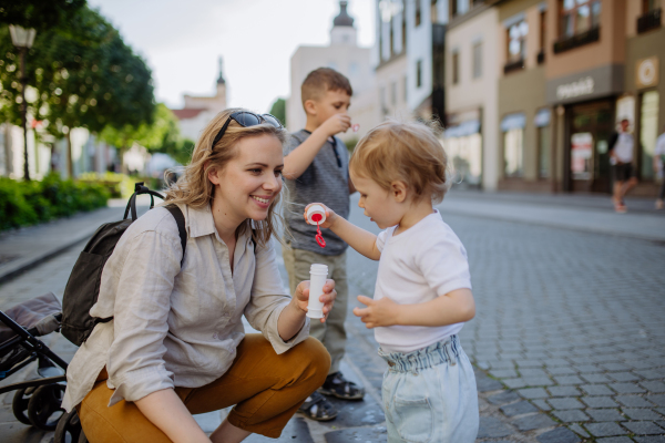 A young mother playing with her kids, blowing bubbles in city street in summer.