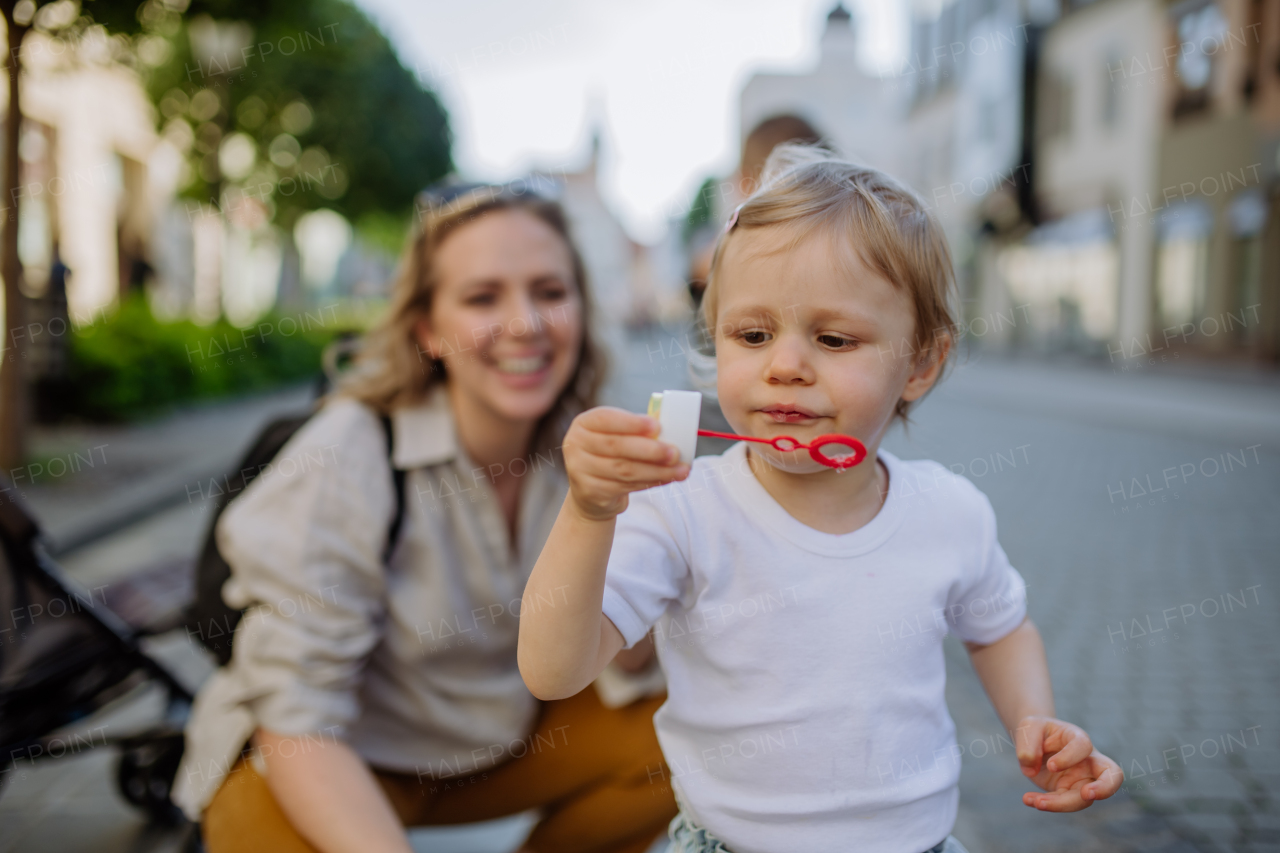 A young mother playing with her kids, blowing bubbles in city street in summer.