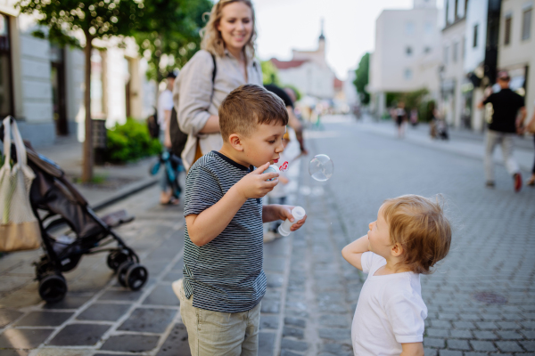 A little boy blowing bubbles with his little sister in city street in summer.