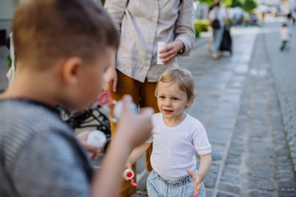 A little boy blowing bubbles with his little sister in city street in summer.