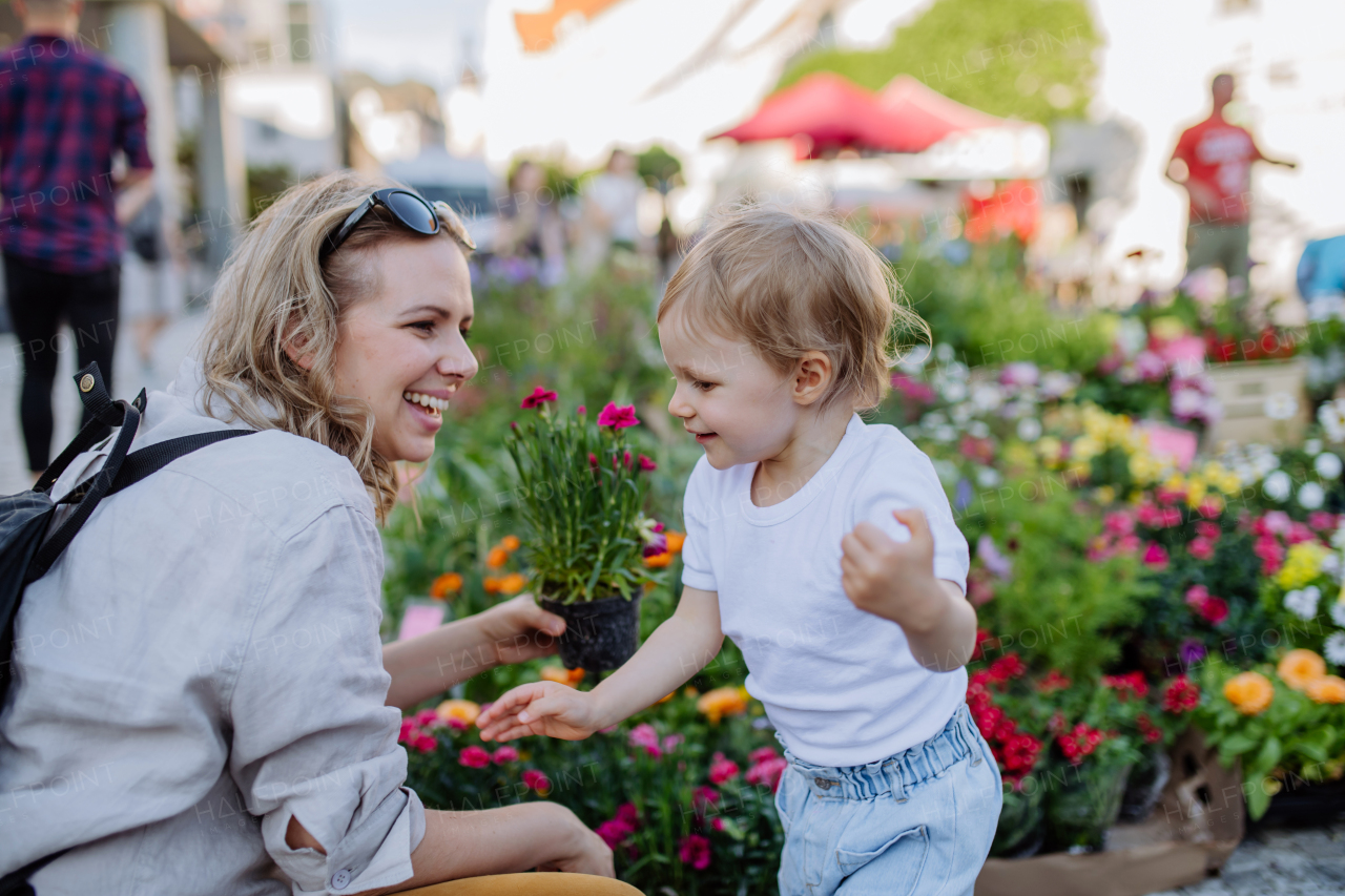 A young mother with her little daughter buying pot flowers in market in summer in city.