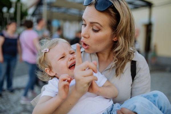 A mother scolding her little daughter in street. Child is crying and woman is shaking finger because of child's bad behavior.