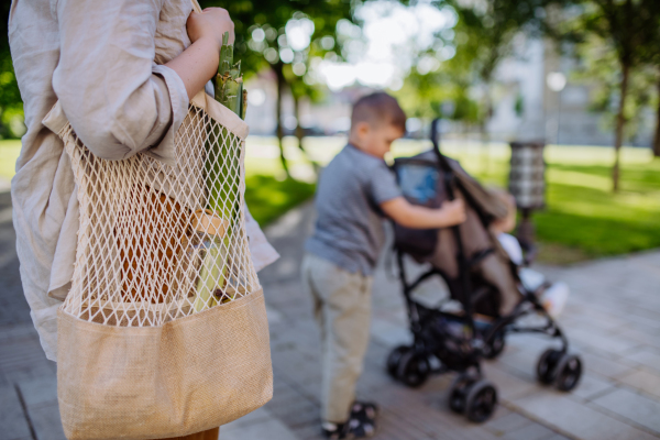 A young mother with zero waste shopping bag with her children and walking in city street, close-up