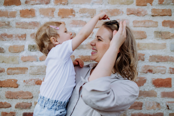 A portrait of young mother with sunglasses holding her little daughter in summer on brick wall background