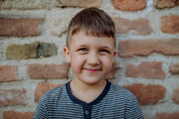 A little boy standing by brick wall and making funny faces in street summer.