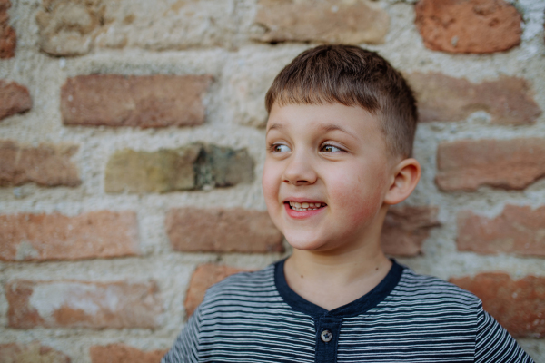 A little boy standing by brick wall and making funny faces in street summer.