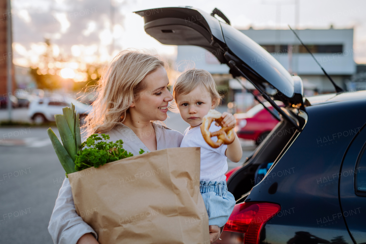 A young mother with little daughter after shopping holding zero waste shopping bags with grocery near car.