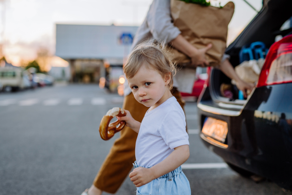 A young mother with little daughter after shopping holding zero waste shopping bags with grocery near car.