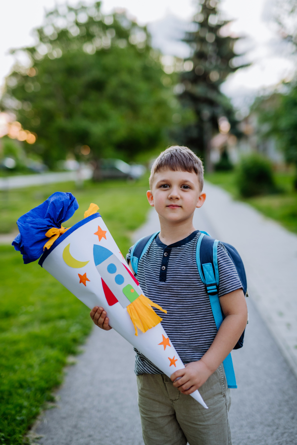 A little kid boy with school satchel on first day of school, holding school cone with gifts