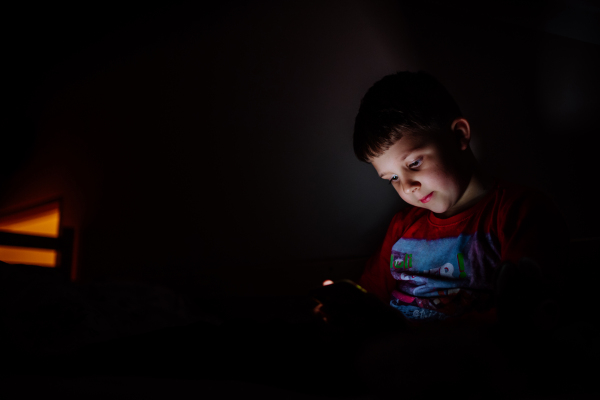 An addicted little boy playing games on phone in bed at night.