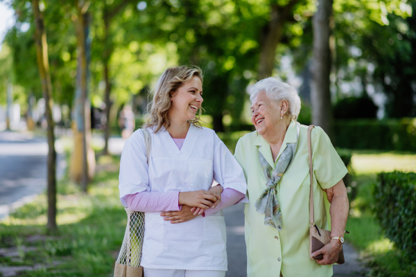 Portrait of caregiver with senior woman on walk in park.