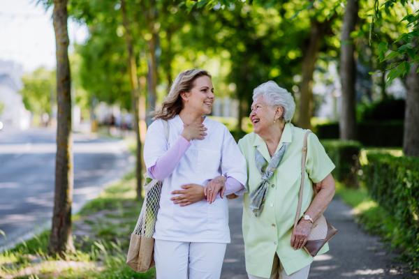 Portrait of caregiver with senior woman on walk in park.