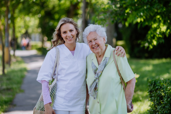 Portrait of caregiver with senior woman on walk in park.