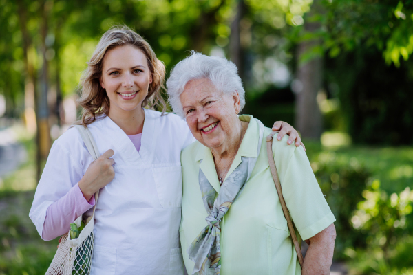 Portrait of caregiver with senior woman on walk in park.